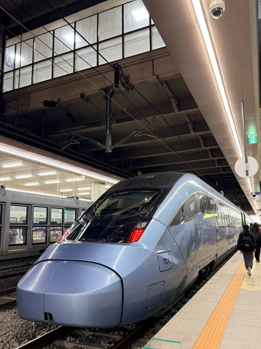 KTX-Eum high-speed train in silver-blue at Cheongnyangni Station platform, photographed head-on with passengers walking alongside behind it