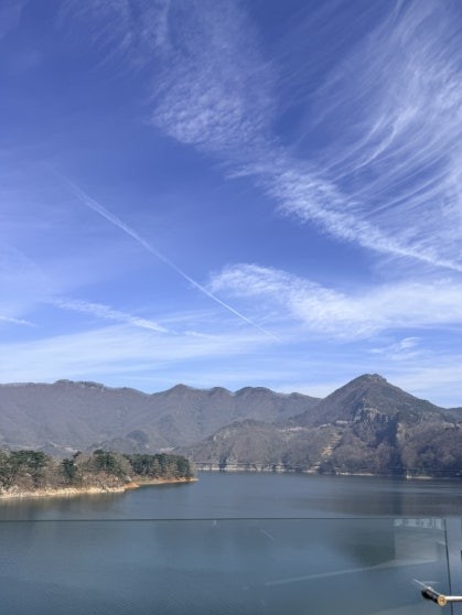 Panoramic view of Okjeongho Lake from a glass-railed vantage point on the suspension bridge, layered mountain ridgelines receding into the distance under a clear blue sky