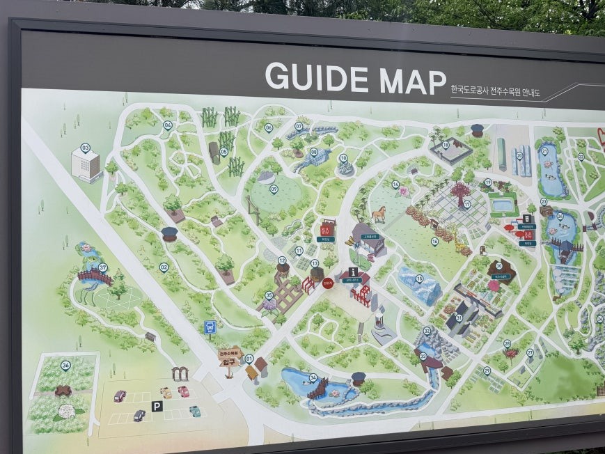 Large outdoor guide map board for Jeonju Arboretum mounted on a dark gray metal frame, showing an illustrated aerial layout of the grounds with multiple numbered garden sections, parking area marked at lower left of the map, and a column of Korean labels on the right